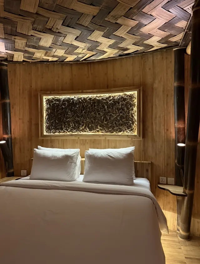 A bed under a woven bamboo ceiling, with a lit recess above the headboard