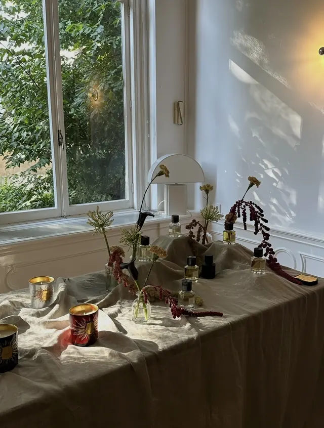 Candles and fragrance bottles arranged on a linen-draped table in low afternoon sun