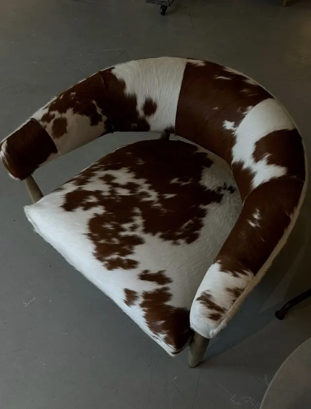 A tub chair upholstered in brown-and-white cowhide on a polished concrete floor