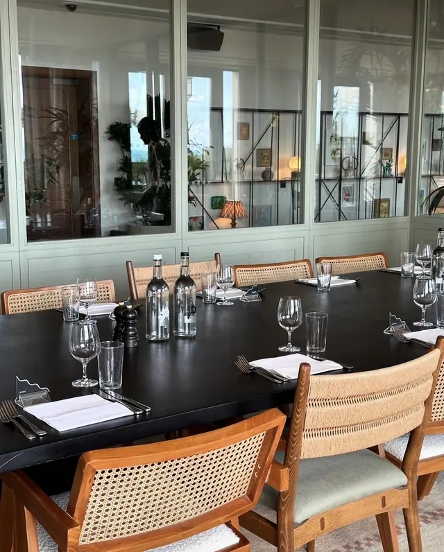 A private dining room laid up on a black table, with cane-backed chairs and a glazed partition