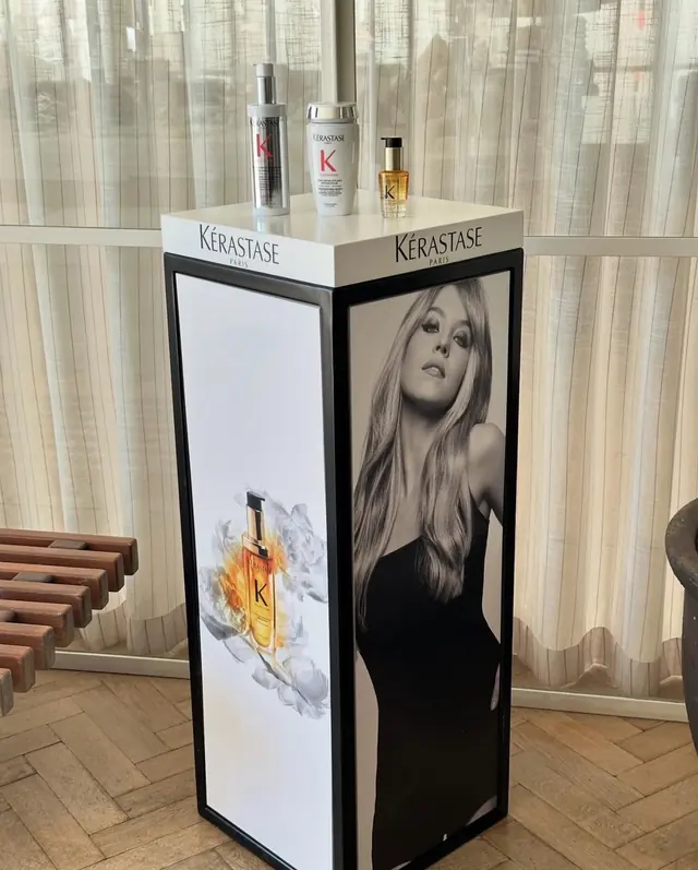 A branded product plinth holding three haircare bottles, in front of sheer curtains