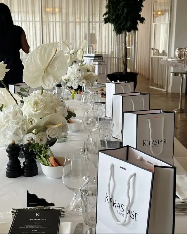 A long table dressed in white for a brand lunch, with white anthuriums and gift bags at every place