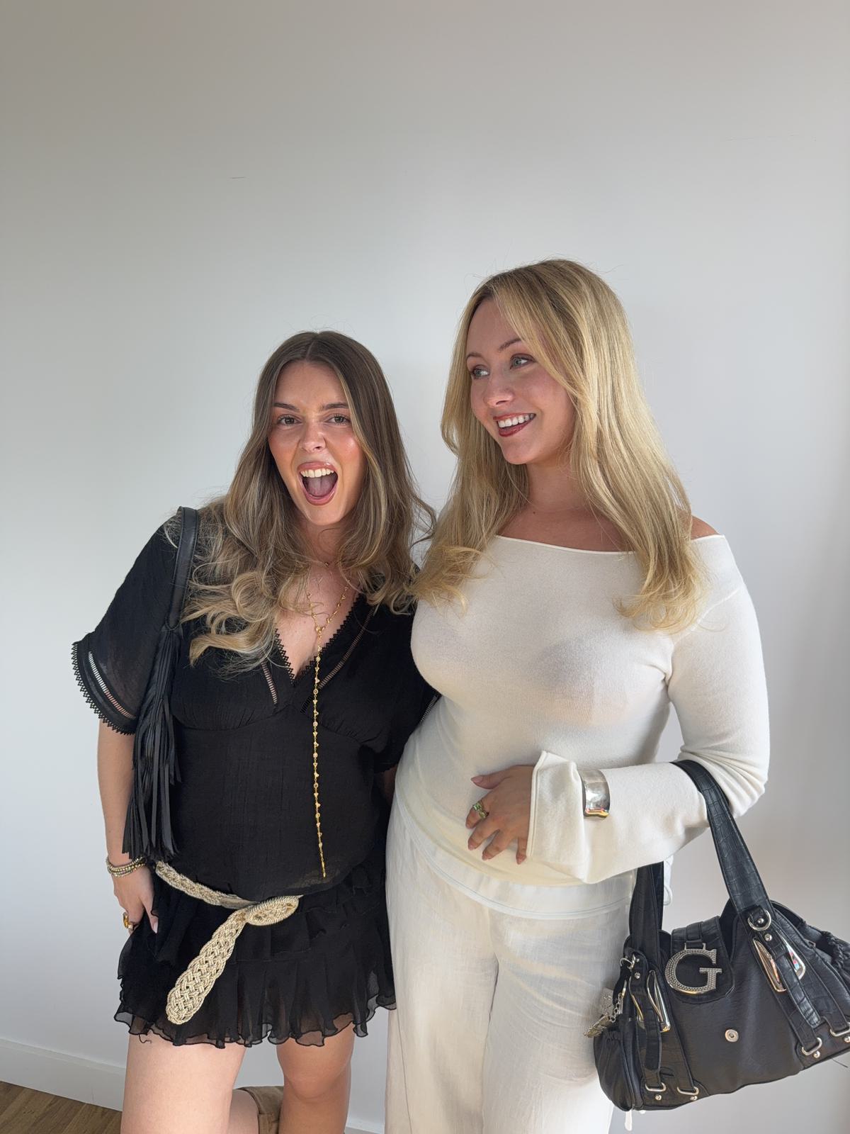 The studio's two founders standing together against a white wall, one in cream, one in black